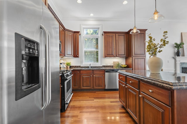 kitchen with appliances with stainless steel finishes, a sink, light wood-type flooring, ornamental molding, and hanging light fixtures