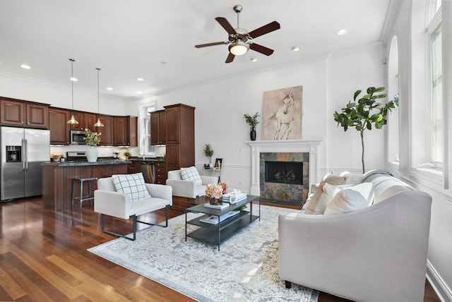 living room featuring dark wood-style flooring, a ceiling fan, a tile fireplace, ornamental molding, and recessed lighting