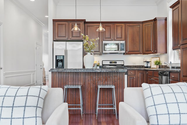 kitchen with appliances with stainless steel finishes, crown molding, a kitchen island, wood finished floors, and pendant lighting