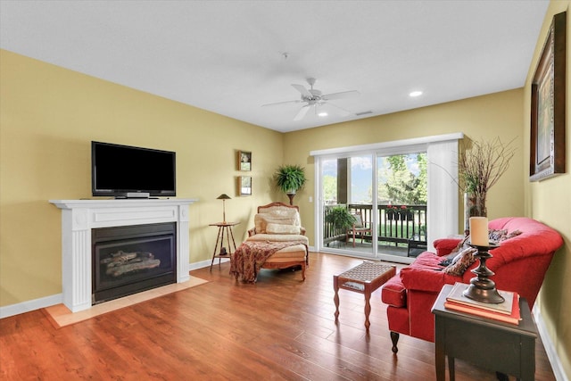 living area featuring a ceiling fan, a fireplace with flush hearth, wood finished floors, baseboards, and recessed lighting