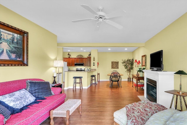 living room with a glass covered fireplace, wood finished floors, baseboards, recessed lighting, and a ceiling fan