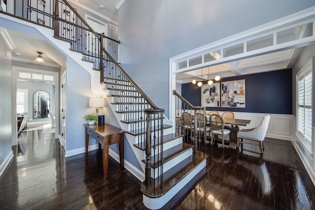 staircase featuring hardwood / wood-style flooring, a chandelier, baseboards, a high ceiling, and ornamental molding