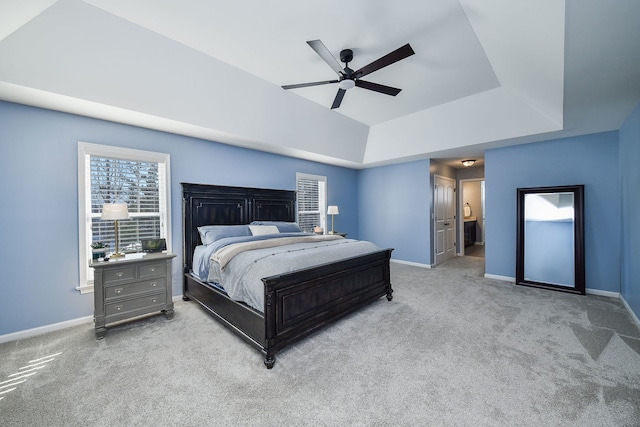 carpeted bedroom featuring ensuite bath, baseboards, ceiling fan, and a tray ceiling
