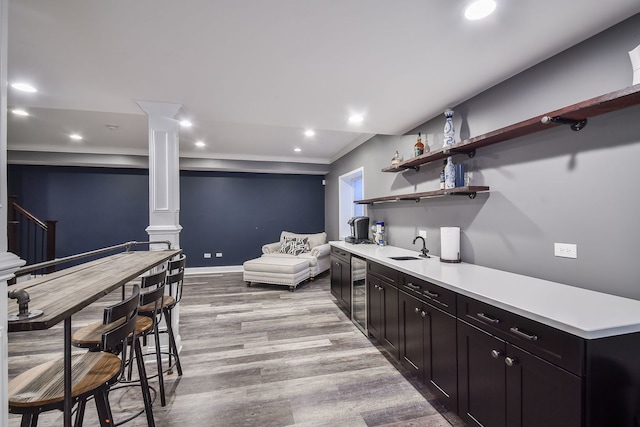 bar with indoor bar, wine cooler, a sink, light wood-style floors, and ornate columns