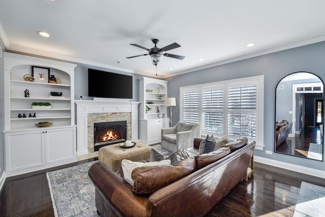 living area with crown molding, a stone fireplace, and a ceiling fan