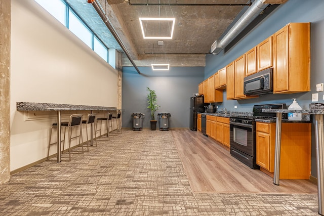 kitchen featuring a high ceiling, light wood finished floors, a sink, and black appliances