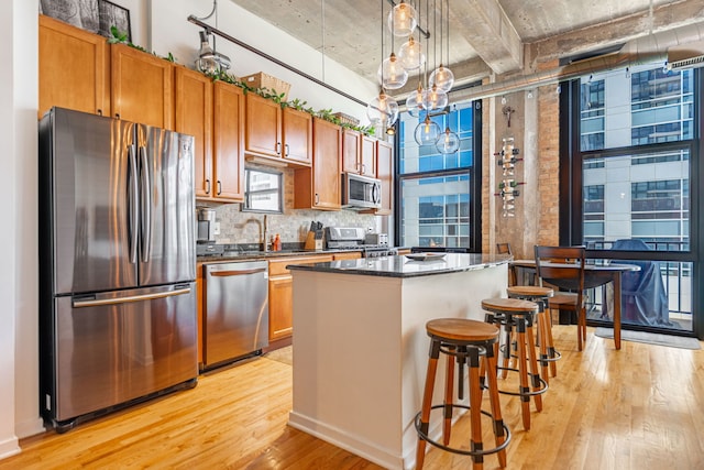 kitchen with decorative backsplash, stainless steel appliances, light wood-style flooring, a notable chandelier, and a kitchen island
