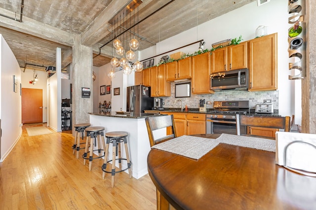 kitchen featuring dark countertops, a breakfast bar, light wood-type flooring, backsplash, and appliances with stainless steel finishes
