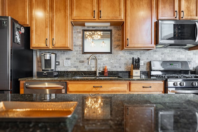 kitchen featuring decorative backsplash, dark stone countertops, stainless steel appliances, and a sink