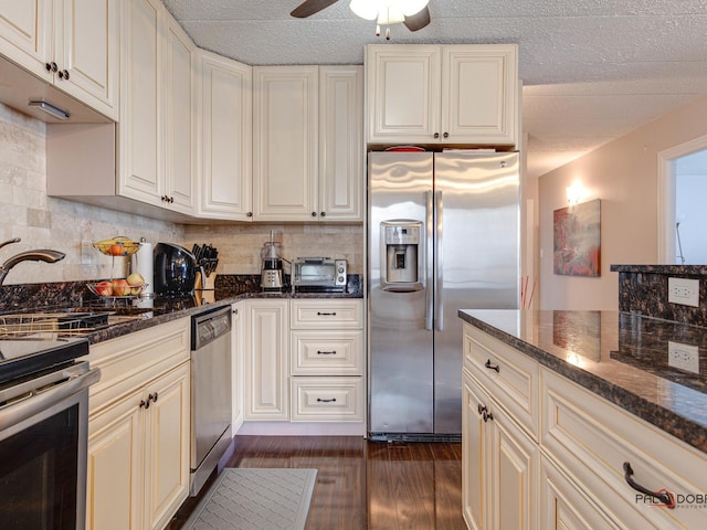 kitchen featuring stainless steel appliances, dark stone countertops, a ceiling fan, dark wood-type flooring, and decorative backsplash