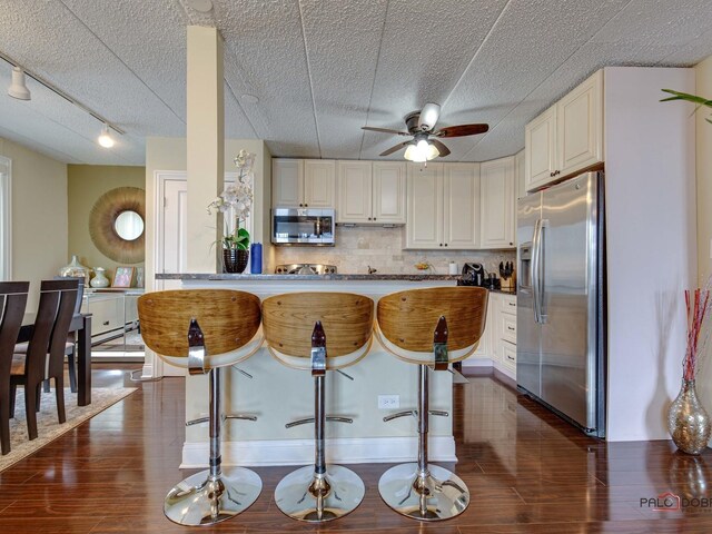 kitchen featuring dark wood-style floors, decorative backsplash, ceiling fan, a breakfast bar, and appliances with stainless steel finishes