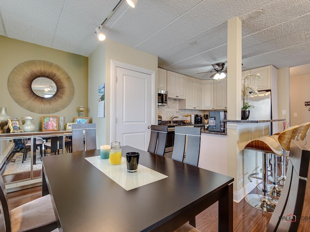 dining area featuring track lighting, wood finished floors, and a ceiling fan