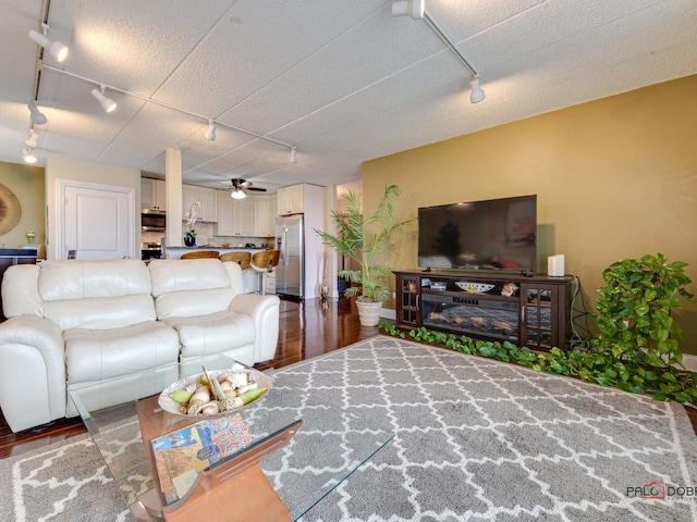 living room with track lighting, wood finished floors, a ceiling fan, and baseboards