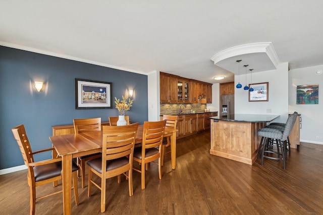 dining space featuring baseboards, crown molding, dark wood-style floors, and indoor wet bar