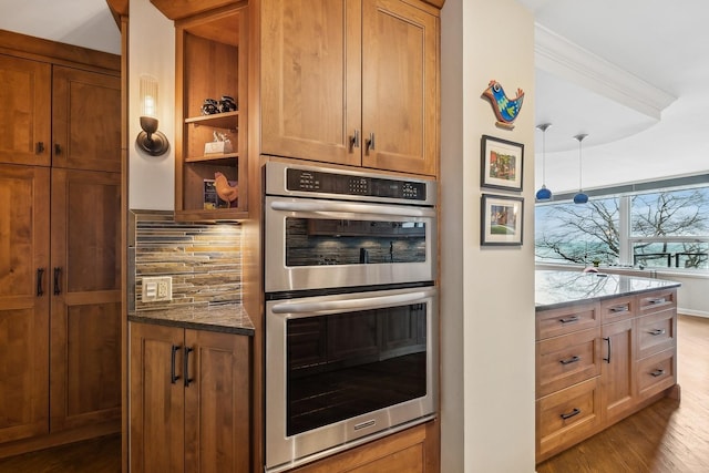 kitchen featuring stainless steel double oven, wood finished floors, brown cabinetry, stone counters, and tasteful backsplash