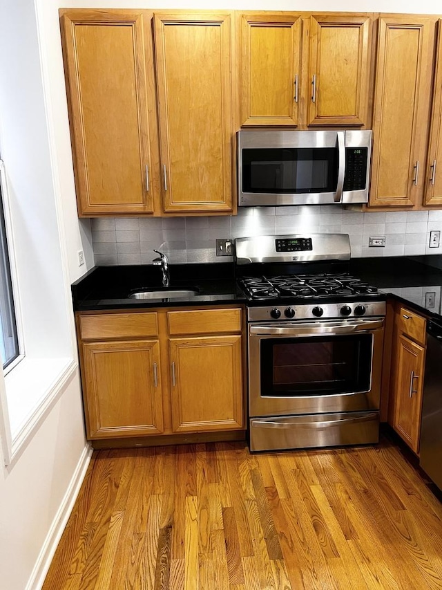 kitchen featuring dark countertops, a sink, backsplash, and stainless steel appliances