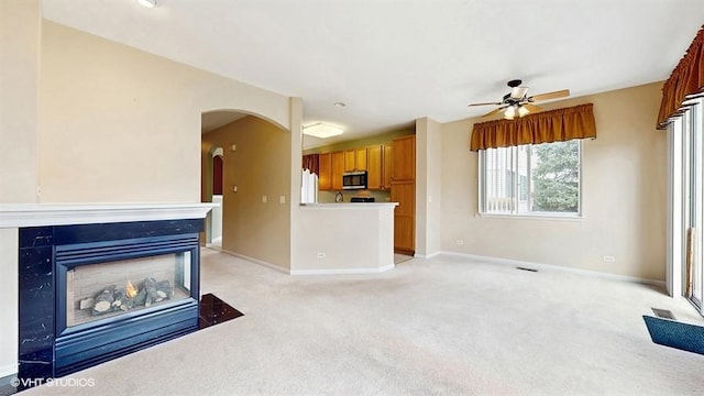 unfurnished living room with visible vents, a ceiling fan, arched walkways, baseboards, and light colored carpet