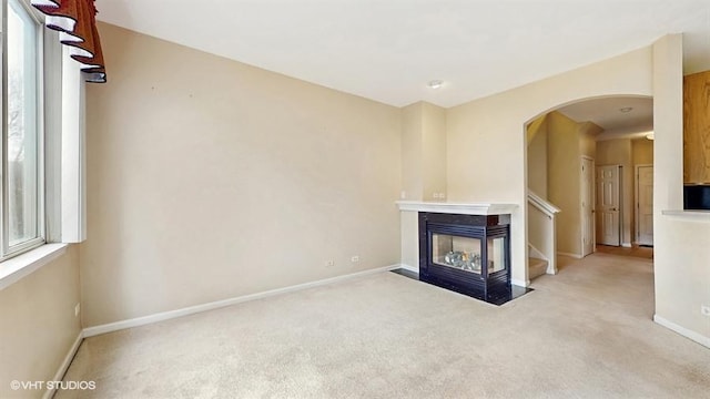 unfurnished living room with arched walkways, carpet, and baseboards