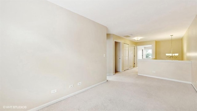 carpeted empty room featuring baseboards and an inviting chandelier
