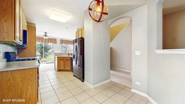kitchen featuring baseboards, light tile patterned floors, a sink, and black fridge