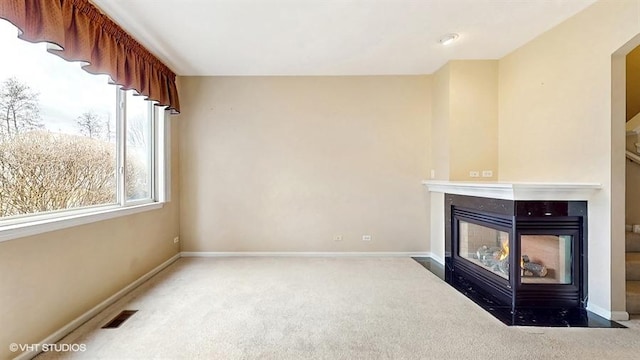 unfurnished living room with carpet floors, a multi sided fireplace, visible vents, and baseboards