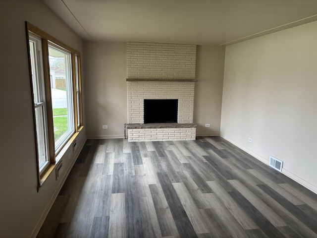 unfurnished living room with a fireplace, baseboards, visible vents, and dark wood-style floors