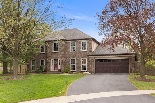 colonial inspired home featuring roof with shingles, brick siding, a garage, aphalt driveway, and a front yard