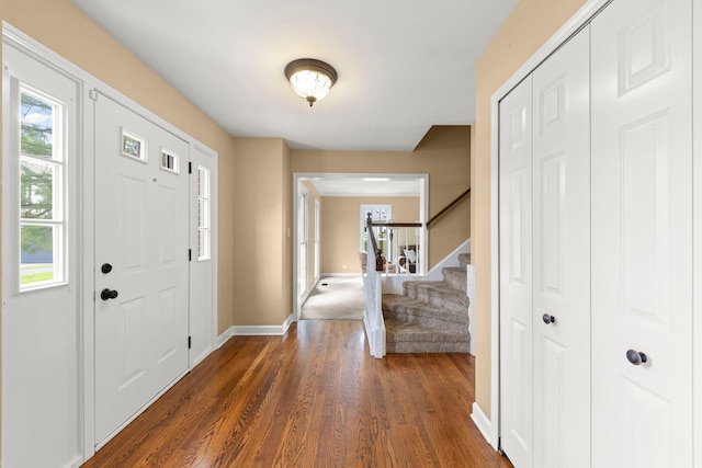 foyer featuring baseboards, stairs, dark wood-style flooring, and a healthy amount of sunlight
