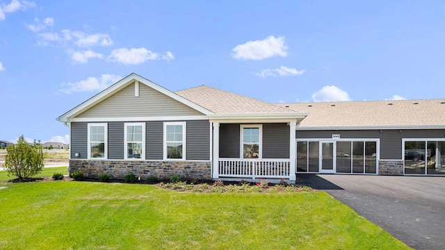 view of front of property featuring covered porch, a front lawn, and stone siding
