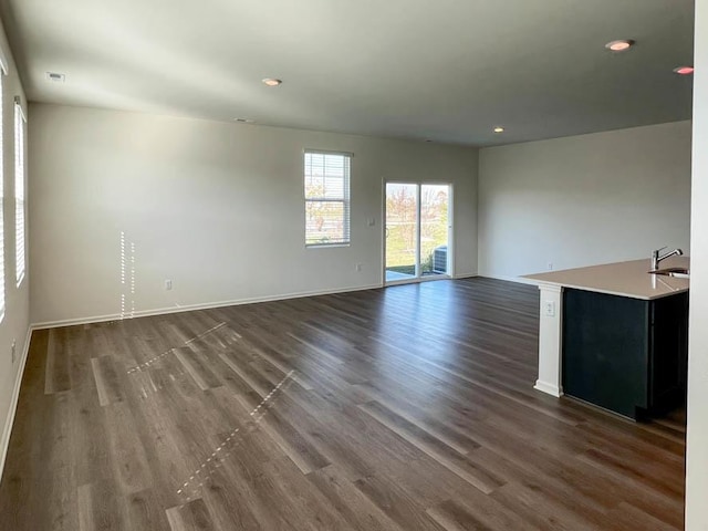 unfurnished living room featuring baseboards, dark wood-style flooring, and a sink