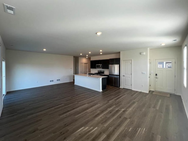 kitchen featuring stainless steel appliances, visible vents, dark wood-type flooring, a center island with sink, and open floor plan