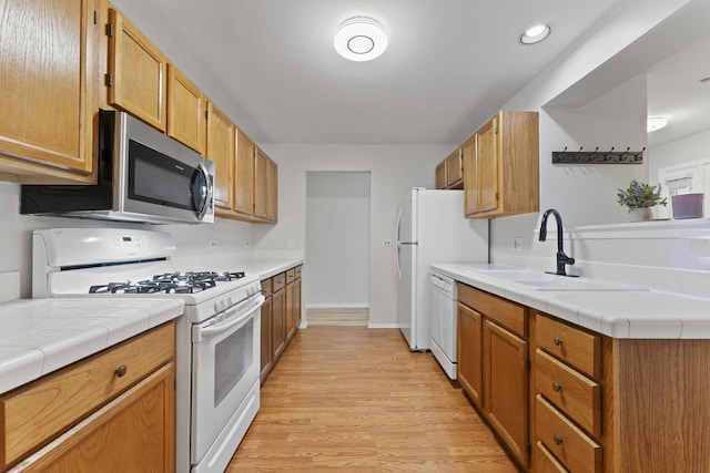 kitchen with a sink, light wood-style floors, tile counters, recessed lighting, and white appliances