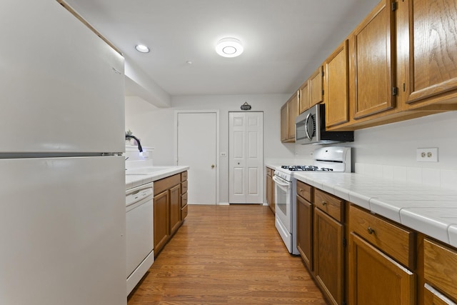 kitchen with white appliances, brown cabinetry, a sink, and light wood-style flooring