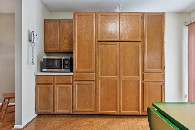 kitchen with brown cabinetry, light wood-style flooring, baseboards, and stainless steel microwave