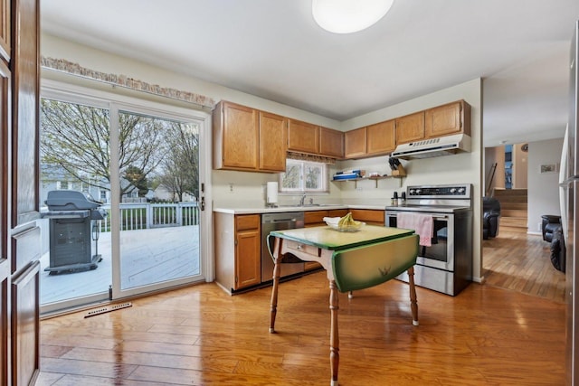 kitchen with stainless steel appliances, under cabinet range hood, a sink, and light wood-style floors