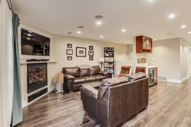 living area with light wood-style flooring, a glass covered fireplace, baseboards, and recessed lighting