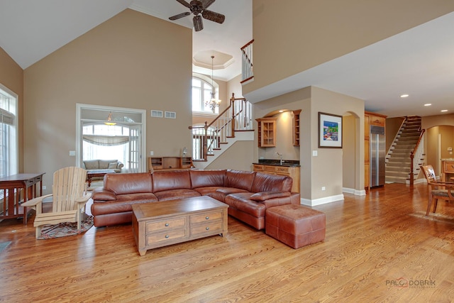 living room with high vaulted ceiling, stairway, arched walkways, a ceiling fan, and light wood-style flooring