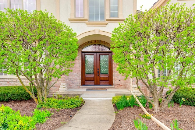 entrance to property featuring french doors, stucco siding, and brick siding