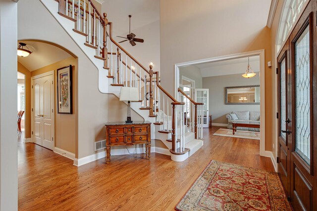 foyer entrance featuring stairway, arched walkways, a ceiling fan, and wood finished floors