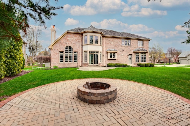 back of house featuring a chimney, a lawn, a patio area, brick siding, and an outdoor fire pit