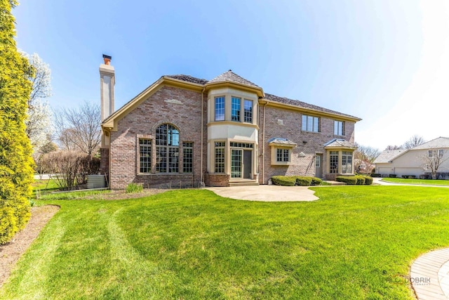 back of property with brick siding, a patio area, a lawn, and a chimney
