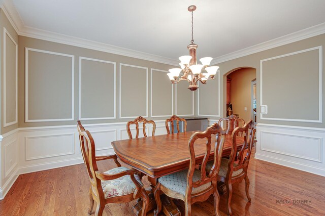 dining area featuring crown molding, arched walkways, a chandelier, and a decorative wall
