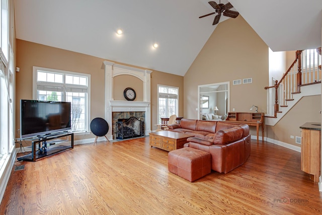 living area featuring ceiling fan, a fireplace, high vaulted ceiling, light wood-style flooring, and baseboards