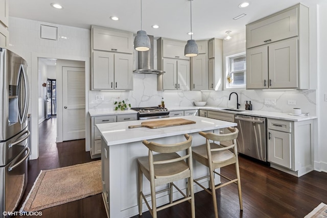 kitchen with wall chimney range hood, appliances with stainless steel finishes, a sink, recessed lighting, and dark wood-type flooring
