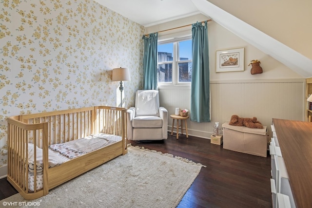 bedroom featuring a nursery area, hardwood / wood-style flooring, wainscoting, and wallpapered walls