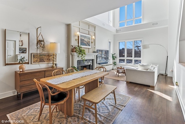 dining area with a lit fireplace, a high ceiling, and hardwood / wood-style floors