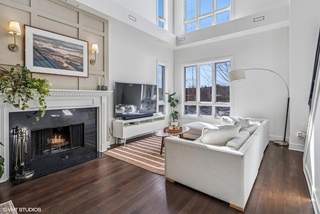 living area with baseboards, a towering ceiling, hardwood / wood-style floors, and a premium fireplace