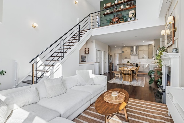 living area with a warm lit fireplace, a high ceiling, stairway, and dark wood-type flooring