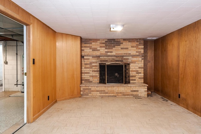 unfurnished living room featuring gas water heater, wooden walls, and a brick fireplace