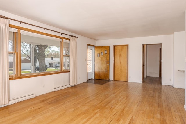 empty room with a baseboard radiator, light wood-type flooring, and baseboards